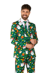 A man dressed in the Suitmeister Santa Elves Green - Christmas suit, which features festive prints of Santa, snowflakes, and gifts. He is smiling while adjusting his jacket with one hand.