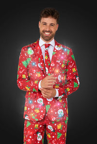 A man wearing the Suitmeister "Christmas Red Icons - Light Up" suit, featuring festive patterns of snowmen, snowflakes, and Christmas trees, is paired with a white shirt and red tie against a dark background.