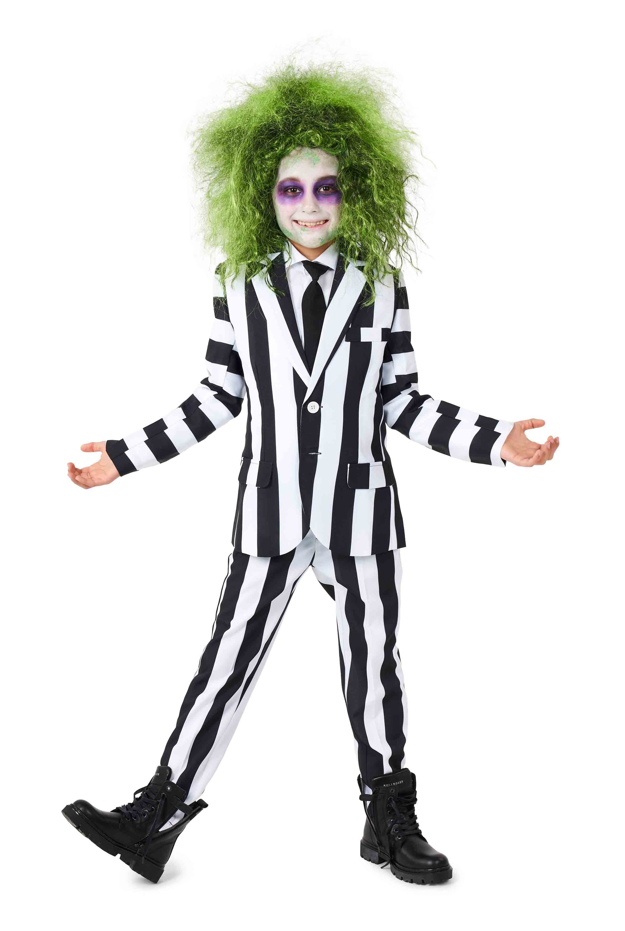A child dressed in a Suitmeister Beetlejuice outfit with wild green hair and white face makeup, smiling with arms outstretched. The makeup features dark eyes and a wide grin. The ensemble is completed with black boots, set against a plain white background.