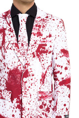 The individual is dressed in a Suitmeister "Bloody Suit White," featuring a white background with red paint splatter details. The shirt underneath is black, and the tie complements the suit by showcasing the same splatter design. Only the upper body is visible.