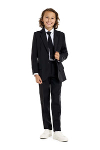A young person with long hair, smiling, is wearing Suitmeisters Solid Black suit paired with a white shirt and black tie, standing against a white background.