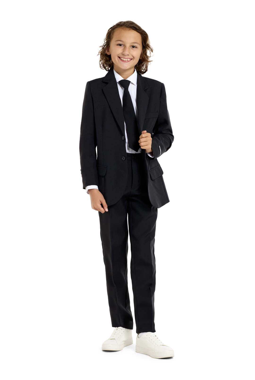 A young person with long hair, smiling, is wearing Suitmeisters Solid Black suit paired with a white shirt and black tie, standing against a white background.