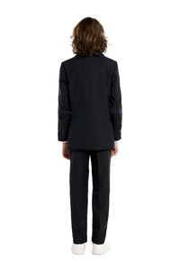 A young person with long hair, smiling, is wearing Suitmeisters Solid Black suit paired with a white shirt and black tie, standing against a white background.