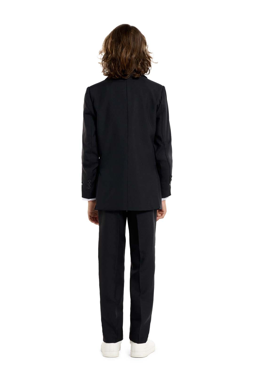 A young person with long hair, smiling, is wearing Suitmeisters Solid Black suit paired with a white shirt and black tie, standing against a white background.