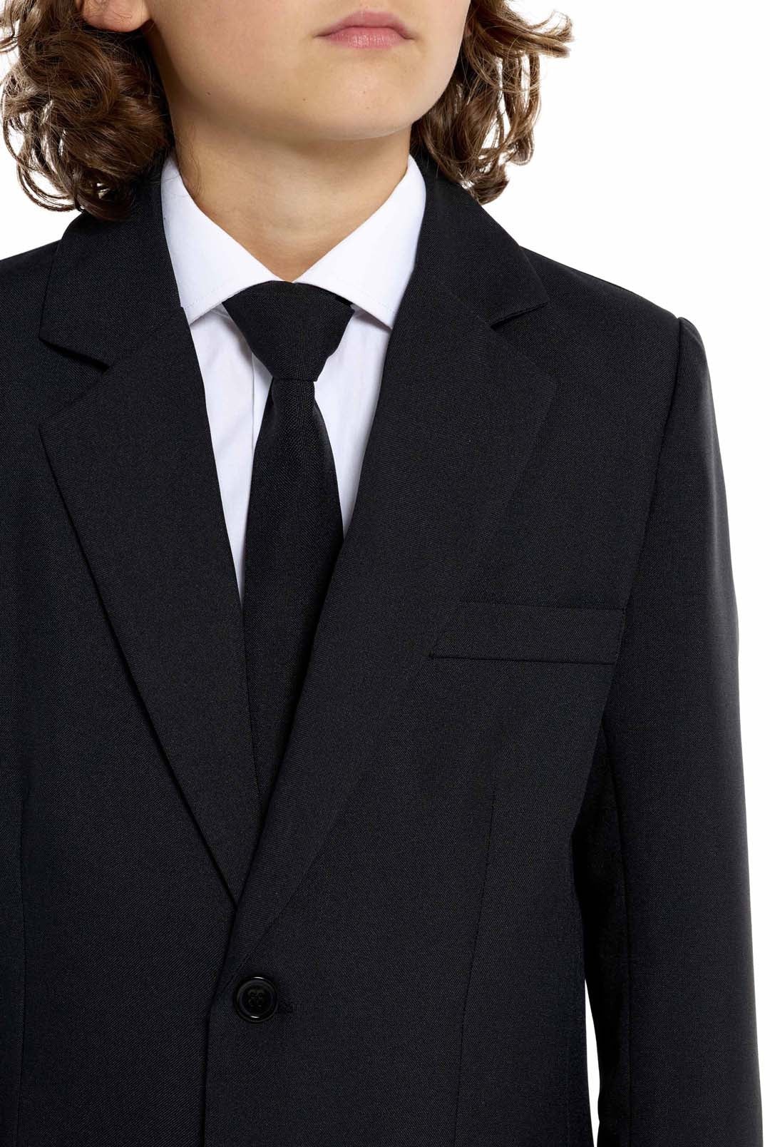 A young person with long hair, smiling, is wearing Suitmeisters Solid Black suit paired with a white shirt and black tie, standing against a white background.