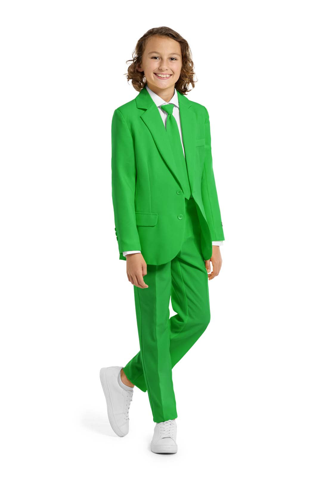 A young person with wavy hair smiles at the camera, wearing a Suitmeister Solid Green suit, white shirt, and green tie. They stand against a white background with one hand in their pocket.