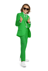 A young person with wavy hair smiles at the camera, wearing a Suitmeister Solid Green suit, white shirt, and green tie. They stand against a white background with one hand in their pocket.