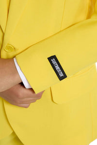 A child with a joyful expression and curly hair is wearing the Solid Yellow suit by Suitmeister, complete with a matching tie, set against a white background.
