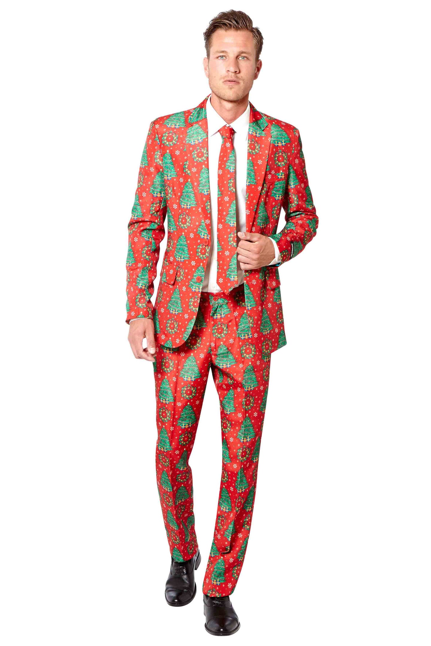 A man dressed in a Suitmeister "Christmas Trees" festive red suit featuring green Christmas trees and snowflakes, paired with a white shirt, matching tie, and black shoes, stands against a plain white background.