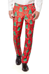 A person is wearing the festive "Christmas Trees" pants by Suitmeister, which feature a pattern of green Christmas trees, snowflakes, and decorative designs. They have paired the pants with a white shirt and black shoes.