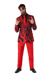 A person dressed in Suitmeister's Devil Red ensemble, featuring black flame patterns on a red background, complemented by a black shirt and red tie, stands against a white backdrop. They are animatedly making the rock hand gesture with both hands.