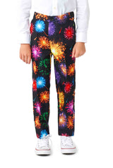 A child is wearing the "Fireworks Black" pants by Suitmeister, featuring a vibrant fireworks pattern in red, orange, blue, and purple. The pants are paired with white sneakers and a white shirt.