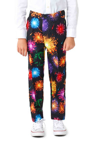 A child is wearing the "Fireworks Black" pants by Suitmeister, featuring a vibrant fireworks pattern in red, orange, blue, and purple. The pants are paired with white sneakers and a white shirt.
