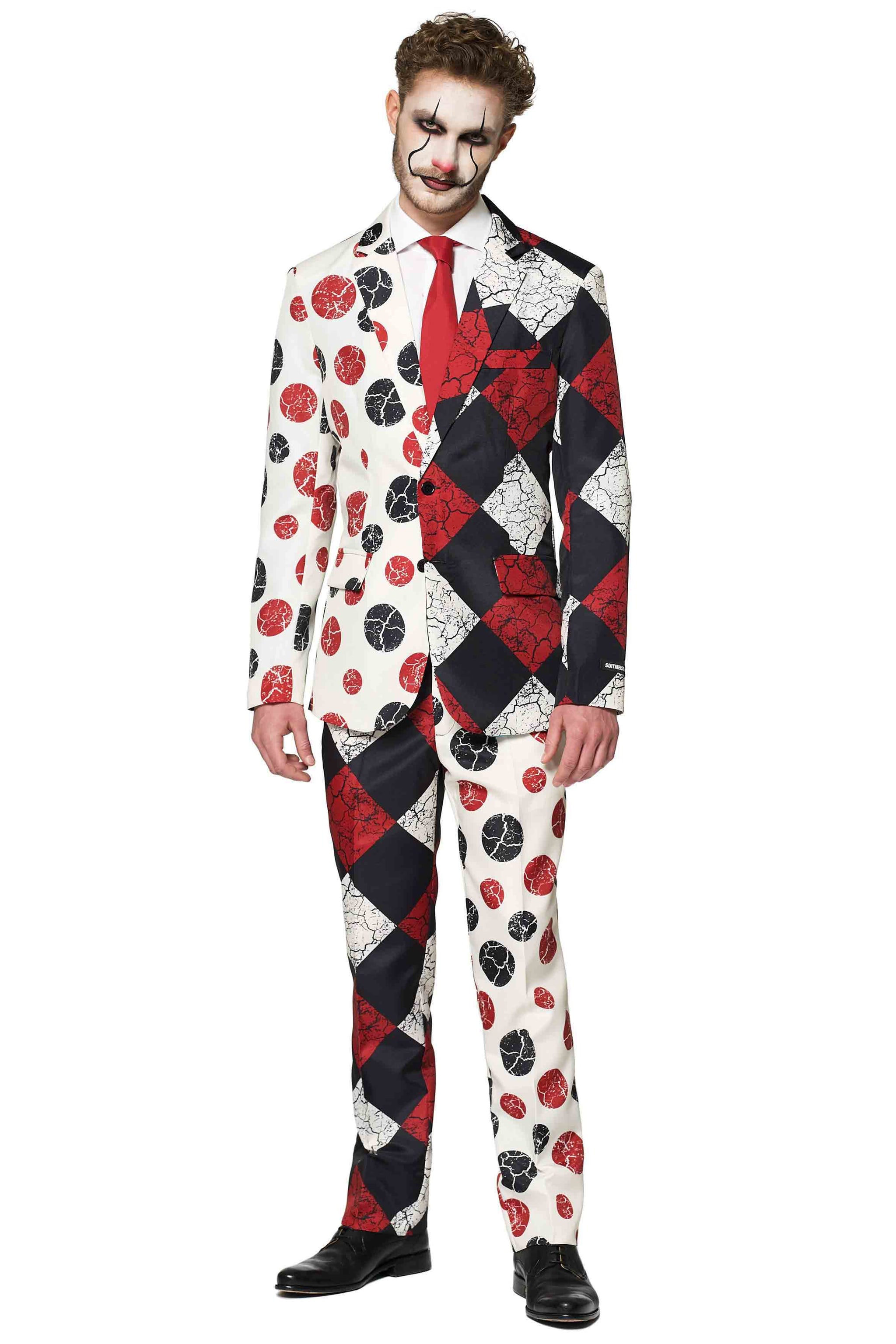 A man is wearing a Halloween Clown Vintage suit by Suitmeister, showcasing a split-pattern design in red, black, and white with circular and checkered motifs. He complements his outfit with clown-like face paint highlighting exaggerated eyes and mouth, paired with a red tie and black shoes.