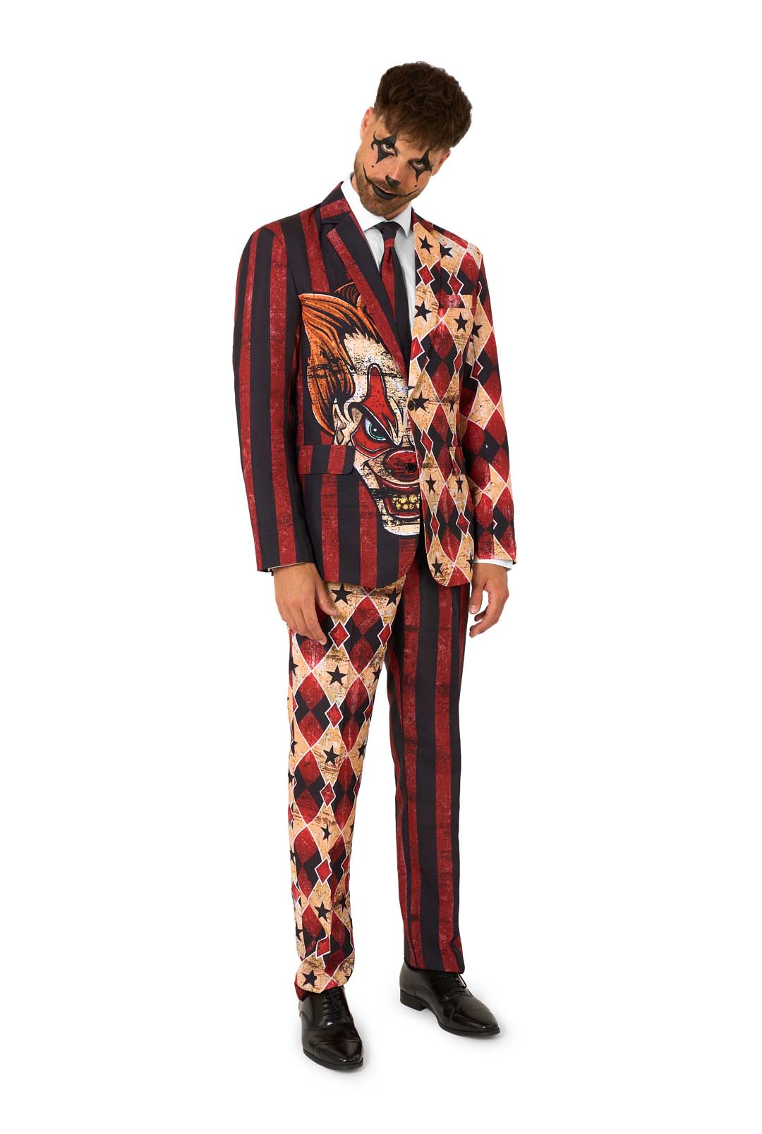 Full-body view of a man in a red and black striped and diamond-patterned suit with clown makeup, tilting his head.