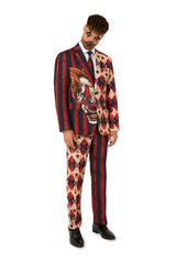 Full-body view of a man in a red and black striped and diamond-patterned suit with clown makeup, tilting his head.