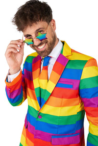 A person smiling and wearing the Suitmeister "Rainbow" suit and tie, with matching glasses. The suit showcases bright horizontal stripes in a spectrum of colors, and the person is adjusting their glasses while looking confidently at the camera.