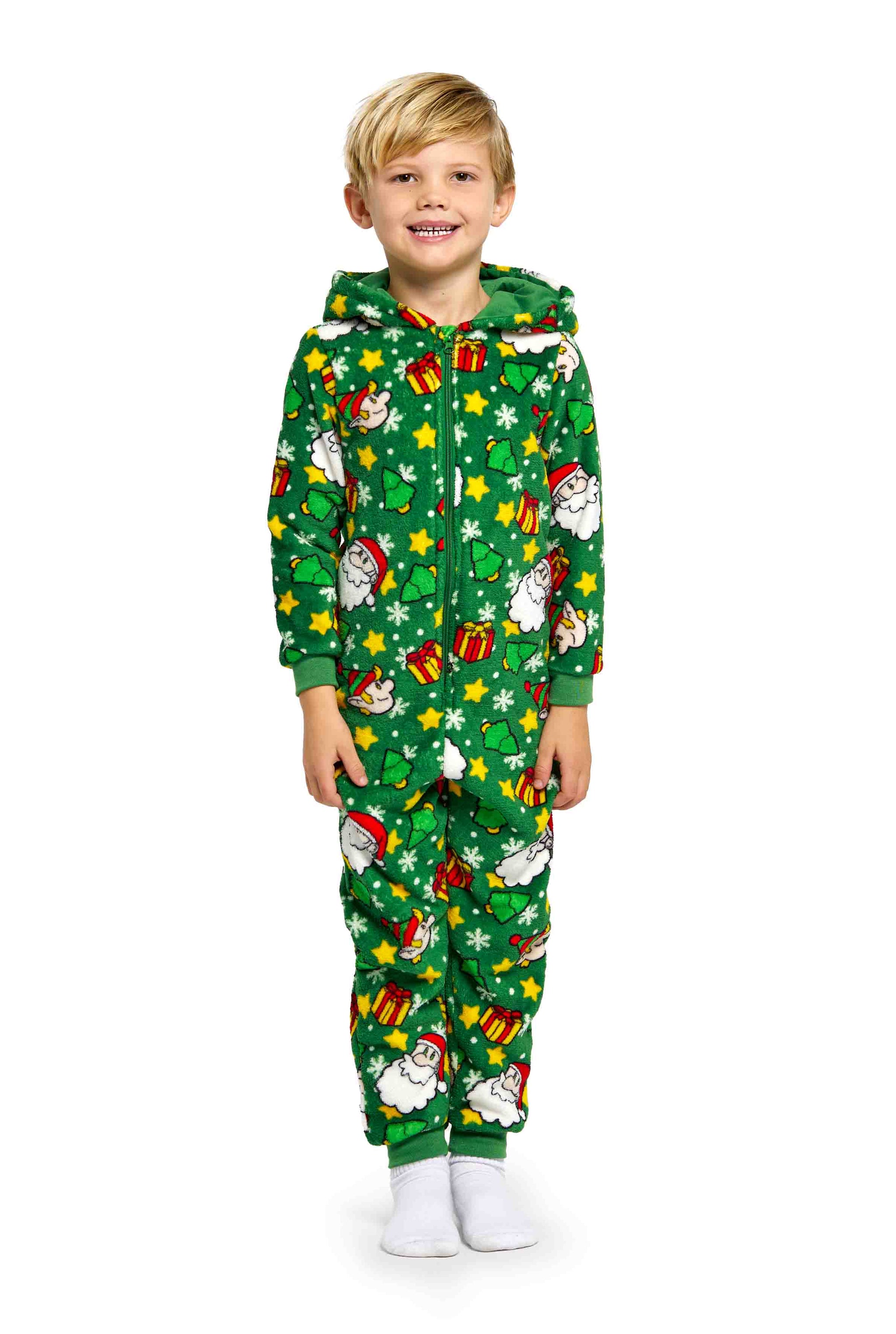 A child wearing the festive Santa Elves Green onesie by Suitmeister smiles happily. The green Christmas-themed outfit, adorned with Santa Claus, candy canes, and gifts, includes a hood and is complemented by white socks.