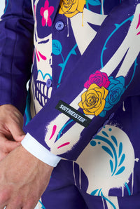 A person is adjusting the cuff of a vibrant, skeleton-themed suit jacket from Suitmeister. The Sugar Skull Purple fabric is adorned with colorful designs, including flowers and skull motifs.