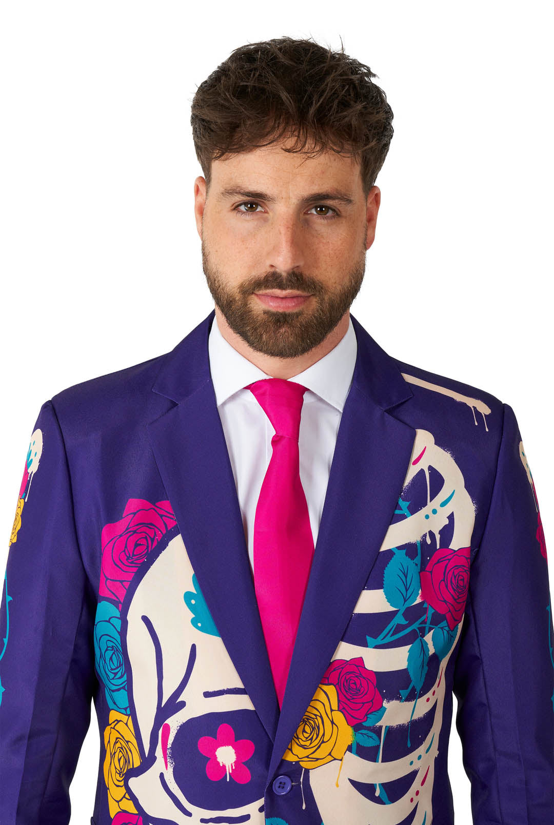 A man with a beard is wearing the Suitmeister "Sugar Skull Purple" suit jacket, decorated with colorful floral and skeleton designs. He has paired it with a white shirt and a bright pink tie, standing against a white background.