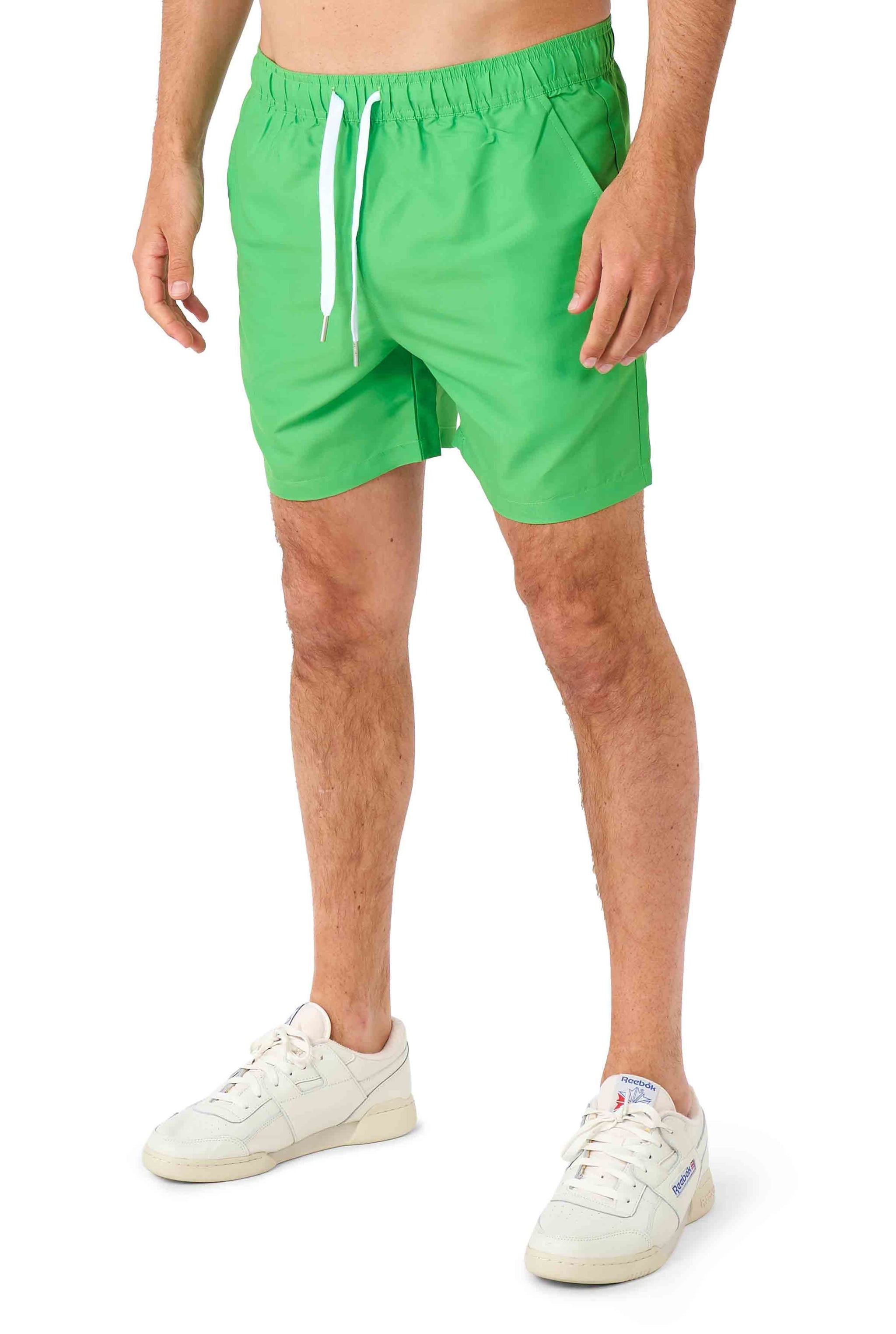 A person is dressed in the TMNT outfit by Suitmeister, featuring vibrant green drawstring shorts, paired with white sneakers. Their legs are visible against a plain white backdrop.